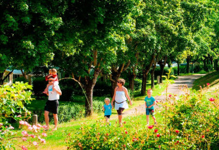 Famiglia che passeggia in un parco verde con alberi a Seasonova Camping Les Rives d'Olt et Aubrac, Occitanie, Francia.