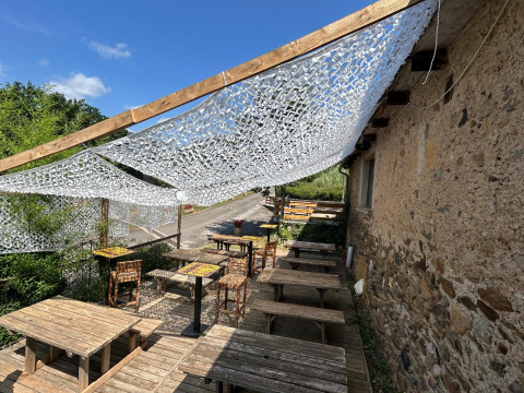 Terrasse extérieure au Seasonova Camping Les Rives d'Olt et Aubrac avec tables en bois et filet d'ombre.