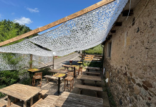 Area esterna con tavoli in legno e copertura ombreggiante a Seasonova Camping Les Rives d'Olt et Aubrac.