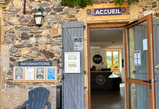 Entrance to the reception at Seasonova Camping Les Rives d’Olt et Aubrac with information board and chair.