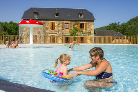 Famiglie si divertono nella piscina bassa al Seasonova Camping Les Rives d'Olt et Aubrac, Occitania, Francia.