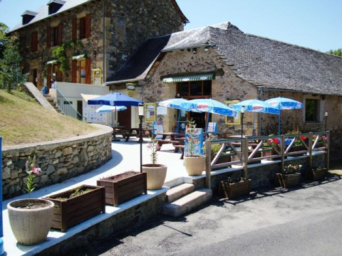 Terrasse extérieure avec tables et parasols au Seasonova Camping Les Rives d'Olt et Aubrac, Occitanie, France.