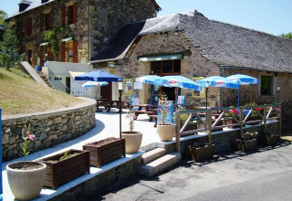 Patio esterno con tavoli e ombrelloni al Seasonova Camping Les Rives d'Olt et Aubrac, Occitanie, Francia.