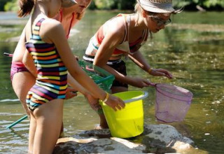 Tre bambini con secchi giocano in un fiume vicino a Seasonova Camping Les Rives d'Olt in Occitania, Francia.