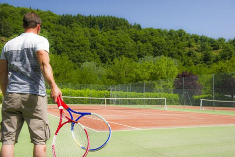 Homme tenant deux raquettes sur un court au Seasonova Camping Les Rives d'Olt et Aubrac, Occitanie, France.