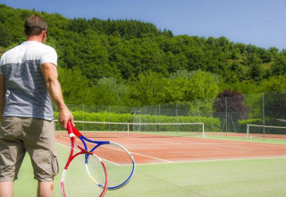 Uomo con due racchette da tennis su un campo presso Seasonova Camping Les Rives d'Olt et Aubrac in Occitania, Francia.