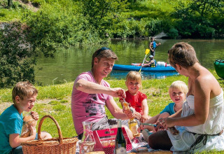 Famille pique-niquant au bord de la rivière au Seasonova Camping Les Rives d'Olt et Aubrac en Occitanie, France.