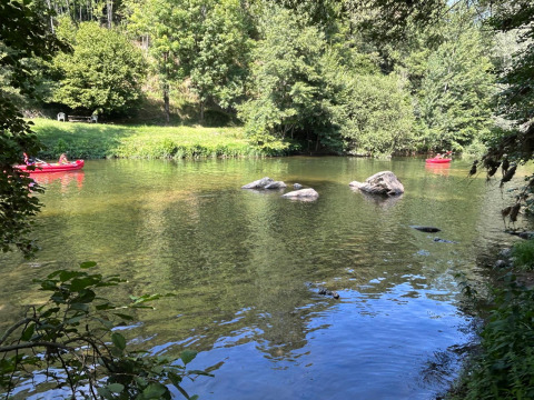 Deux canoës rouges sur une rivière tranquille, entourée de verdure, au Seasonova Camping Les Rives d'Olt en Occitanie.