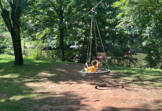 Un enfant repose sur une balançoire ronde sous les arbres près d'une rivière à Seasonova Camping Les Rives d'Olt et Aubrac, France.