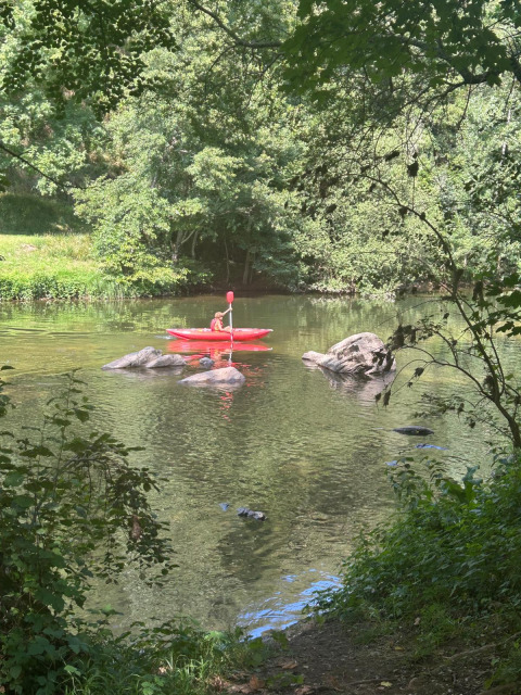 Persona in kayak rosso che rema su un fiume al Seasonova Camping Les Rives d'Olt et Aubrac in Occitania, Francia.