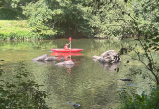 Personne en kayak rouge pagayant sur la rivière au Seasonova Camping Les Rives d'Olt et Aubrac, Occitanie, France.