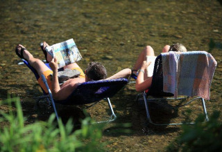 Zwei Personen entspannen auf Stühlen im Fluss bei Seasonova Camping Les Rives d'Olt et Aubrac, Occitanie.