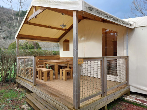 Safari-Zelt Lodge Confort mit überdachter Holzterrasse, Holzmöbeln und Ausblick auf die Natur.