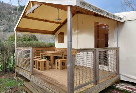 Safari-Zelt Lodge Confort mit überdachter Holzterrasse, Holzmöbeln und Ausblick auf die Natur.