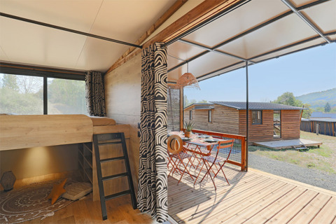 Interno del Tiny Lodge al Seasonova Camping Les Rives d'Olt et Aubrac in Francia, con terrazza e tavolo all'aperto.