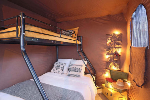 Vista interna della Tiny Lodge con letto a castello, luci soffuse e cuscini in un campeggio in Francia.