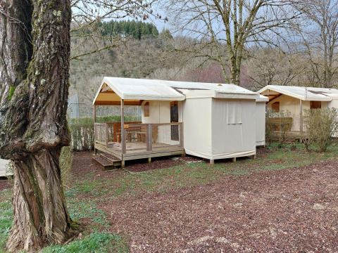 Safari-Zelt Lodge Confort auf dem Seasonova Camping Les Rives d'Olt et Aubrac, inmitten von Bäumen.