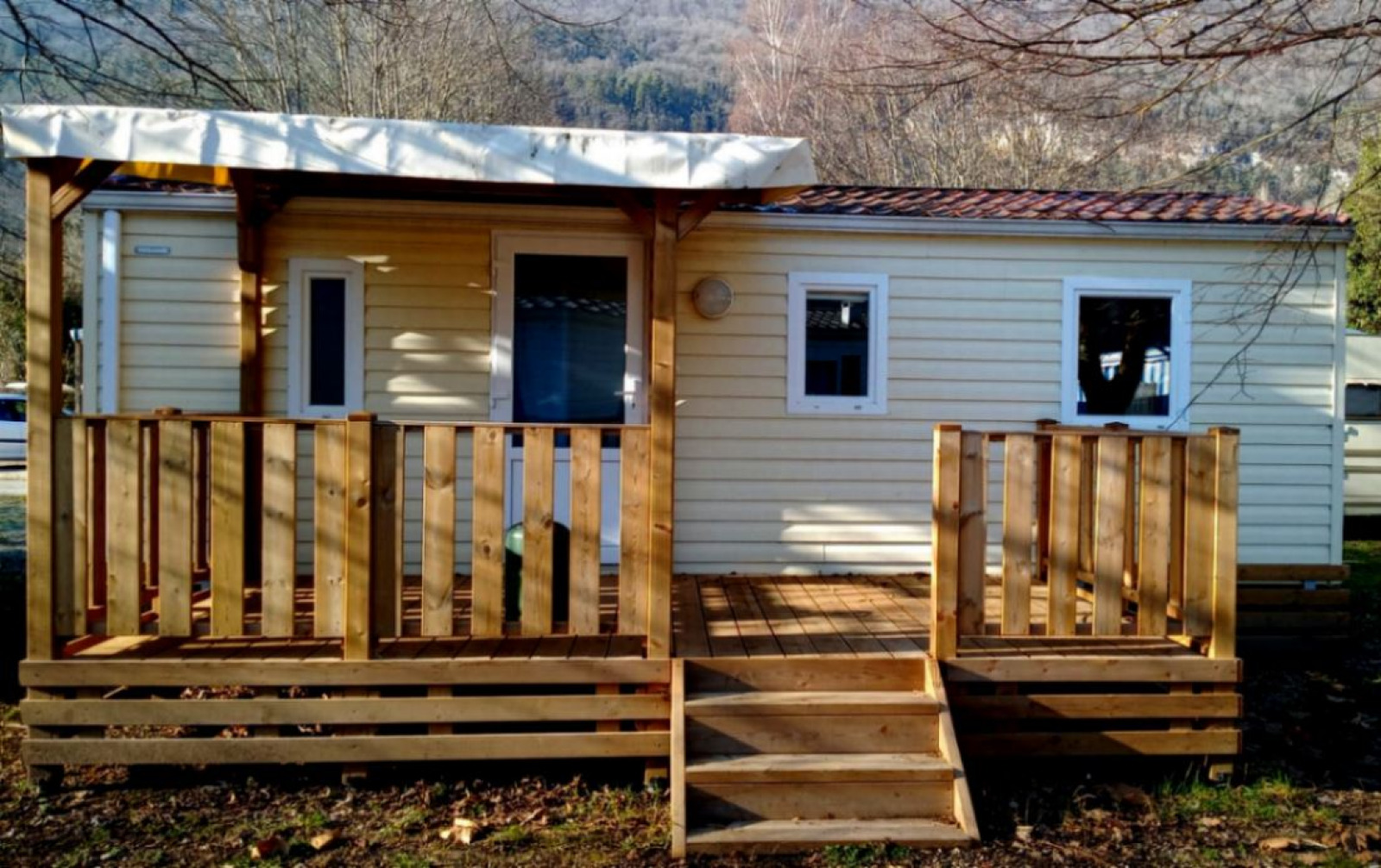 Een foto van een glampingverblijf met een mobiele cabin, houten veranda en een natuurlijke omgeving.