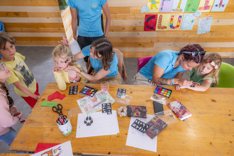 Kinder und Betreuer machen Gesichtsbemalung und Basteln im Seasonova Camping Le Val de Coise in Frankreich.
