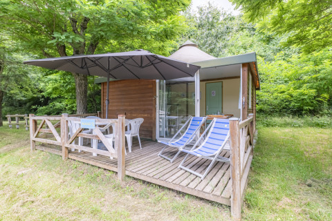 Gemütliche Holzhütte mit Terrasse, Liegestühlen und Sonnenschirm im Grünen im Seasonova Camping.