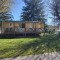 Mobile Home Eco met veranda en stoelen op zonnig grasveld, omringd door bomen en groen.
