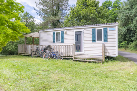 Sistemazione glamping con casa mobile, veranda in legno e biciclette, immersa nella natura verde.