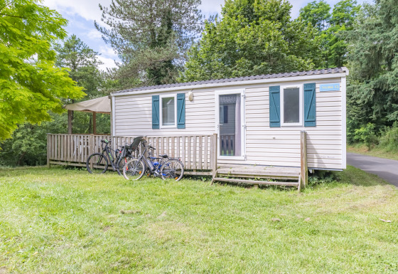 Sistemazione glamping con casa mobile, veranda in legno e biciclette, immersa nella natura verde.
