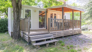 En glampingbolig med overdækket træterrasse under træer, perfekt til en afslappende ferie i naturen.