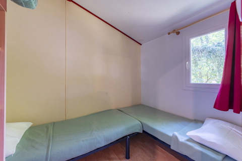 Room with two single beds, green covers, a window, and red curtain at Mobile Home Eco in France.