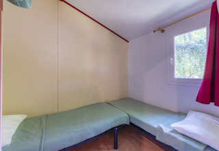 Chambre avec deux lits simples, couvertures vertes et fenêtre à rideau rouge au Mobile Home Eco en France.