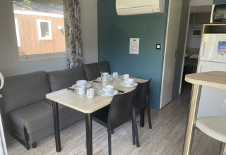 Zona pranzo con divano grigio e tavolo apparecchiato per quattro nel mobilhome Comfort+ al Seasonova Camping Le Val de Coise, Francia.