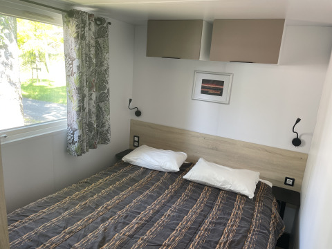 Camera da letto nella casa mobile Comfort+ al Seasonova Camping Le Val de Coise, con letto matrimoniale e finestra.