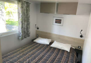 Camera da letto nella casa mobile Comfort+ al Seasonova Camping Le Val de Coise, con letto matrimoniale e finestra.