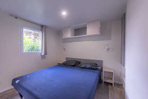Premium Mobilheim-Schlafzimmer mit großem Bett, blauer Bettwäsche, Fenster und modernen Möbeln in Frankreich.