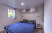 Camera da letto di casa mobile premium con letto grande, biancheria blu e finestre in campeggio francese.