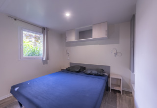 Premium Mobilheim-Schlafzimmer mit großem Bett, blauer Bettwäsche, Fenster und modernen Möbeln in Frankreich.