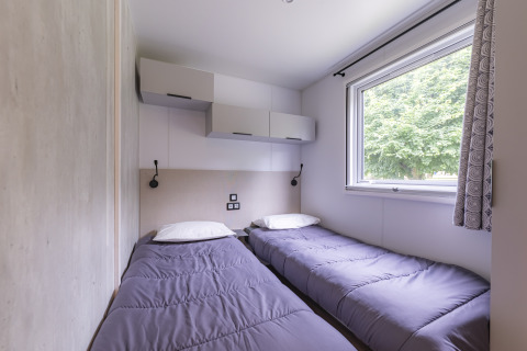 Twin bedroom with two single beds and a window in a Premium mobile home at Seasonova Camping Le Val de Coise, France.