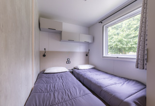 Dormitorio con dos camas individuales y ventana en casa móvil Premium del Seasonova Camping Le Val de Coise, Francia.