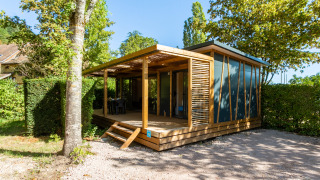 Eine moderne Glamping-Unterkunft mit Holzveranda im Grünen, umgeben von Bäumen und Sonnenlicht.
