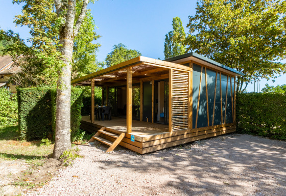 Alojamiento de glamping moderno con terraza de madera y rodeado de árboles en un entorno natural.