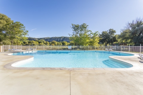 Udendørs swimmingpool i feriestedet Seasonova Camping Les Prés du Verdon, omgivet af træer og bakker.