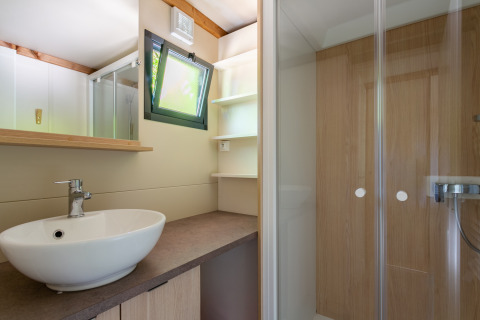Baño moderno con lavabo, espejo, ducha y ventana en Cottage Comfort, Camping Paradis Le Giessen, Francia.