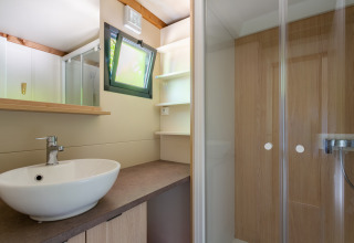 Moderne badeværelse med vask, spejl, bruser og vindue på Cottage Comfort i Camping Paradis Le Giessen, Frankrig.