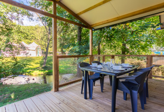 Træterrasse med spisebord og stole ved Camping Paradis Le Giessen, med udsigt over grønt og en å.
