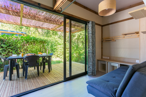 Sala luminosa con acceso a terraza de madera en Cottage Premium, Camping Paradis Le Giessen, Francia.