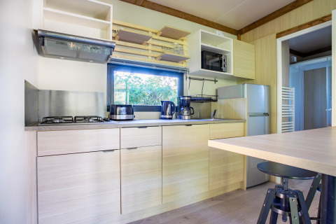 Cocina moderna en Cottage Premium del Camping Paradis Le Giessen en Francia, con muebles y electrodomésticos claros.
