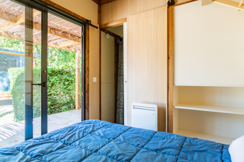 Slaapkamer in Cottage Premium bij Camping Paradis Le Giessen, Frankrijk, met uitzicht op terras en tuin buiten.