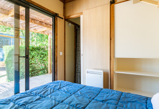 Slaapkamer in Cottage Premium bij Camping Paradis Le Giessen, Frankrijk, met uitzicht op terras en tuin buiten.