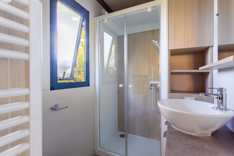 Baño moderno con ducha de vidrio, lavabo redondo y ventana abierta en Cottage Premium, Camping Paradis Le Giessen.