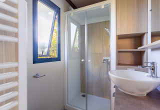 Baño moderno con ducha de vidrio, lavabo redondo y ventana abierta en Cottage Premium, Camping Paradis Le Giessen.
